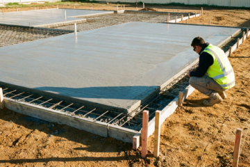 Site supervisor in hi-vis inspecting the corner of a newly poured concrete slab with exposed steel mesh and survey pegs