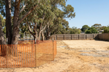 Suburban building block with native gum trees fenced by orange safety mesh and a cleared building pad beyond